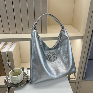 Sac fourre-tout argenté métallisé avec chaîne et logo M sur une étagère minimaliste
