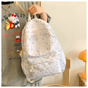 Detail of white canvas backpack with blue stars and cute plush pendant in home setting
