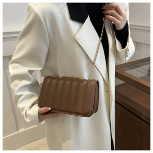 Detail of dark brown quilted chain shoulder bag worn with white suit blazer
