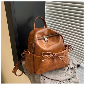 Détail d'un sac à dos marron en similicuir avec décoration de nœud et fermeture éclair