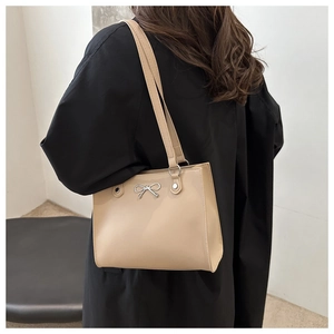 Detail of beige tote bag with silver bow ornament worn with a black wool coat