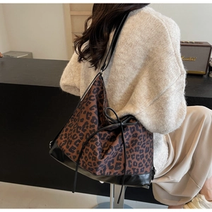 Detail of large leopard print tote bag with drawstring, worn over the shoulder by a model