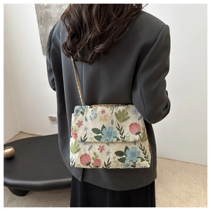 Detailed embroidery of colorful flowers on a cream corduroy shoulder bag with gold chain