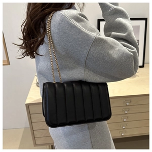 Detail of a black quilted chain crossbody bag styled with a casual grey sweatshirt