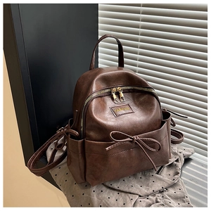 Détail d'un sac à dos en cuir marron foncé avec un nœud vintage et une plaque métallique