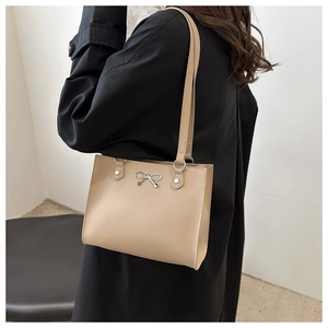 Detail of a beige tote bag featuring thin shoulder straps and a silver metal bow buckle