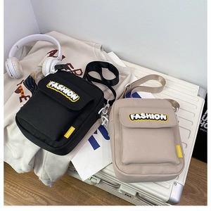 Detail of canvas crossbody bags in black and beige with FASHION embroidery on a suitcase