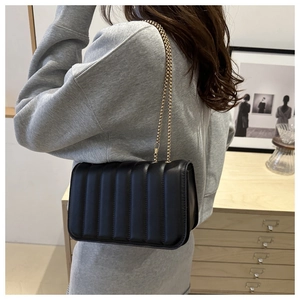 Detail of a black puffy quilted shoulder bag with elegant golden chain strap for women