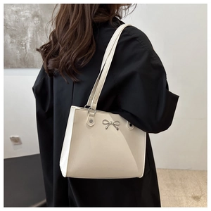 Detail of a creamy white tote bag featuring a silver metal bow accent and slim straps