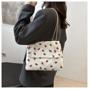 Corduroy crossbody bag with strawberry print and gold chain strap shown on model