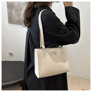 Close-up of cream minimalist tote bag featuring a decorative silver metal bow detail