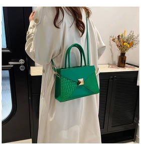 Detail of green envelope bag featuring gold square rivets and crocodile pattern texture