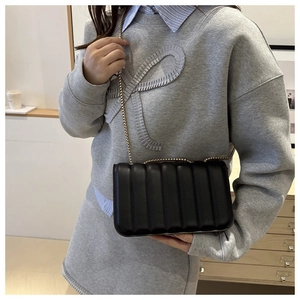 Detail of black pleated crossbody bag with a golden metal chain strap on model
