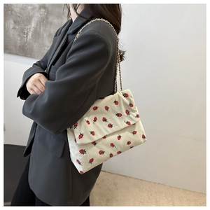 Detail of strawberry corduroy crossbody bag with golden chain strap on a model