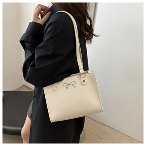 Detail of beige tote bag showing silver metal bow buckle and smooth faux leather texture