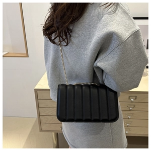 Detailed back view of a black quilted crossbody bag with gold chain strap on grey hoodie