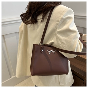 Detail of a brown matte leather tote bag featuring a silver bow accent and slim strap