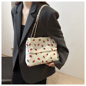 Detail view of white corduroy shoulder bag with strawberry print and gold chain strap