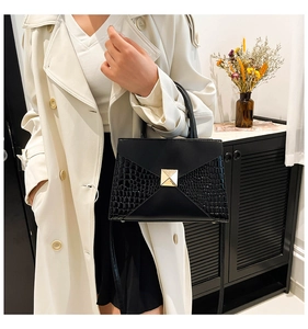 Detail of black trapezoid handbag with gold pyramid stud and crocodile texture trim