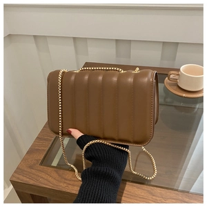 Detail of a brown quilted leather shoulder bag with elegant gold chain strap in a cafe setting