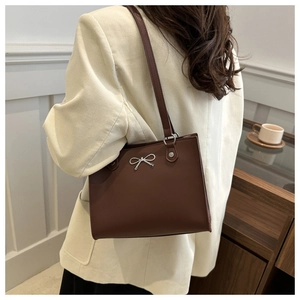 Close-up of dark brown tote bag featuring a silver metal bow accent and slim shoulder straps