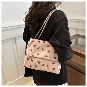 Detail of pink corduroy crossbody bag with strawberry embroidery and golden chain strap