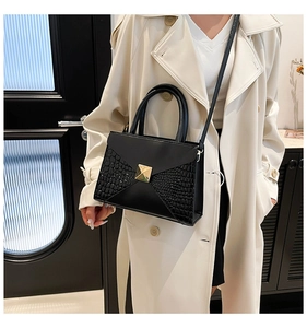 Detail of black faux crocodile leather handbag with gold buckle on beige trench coat