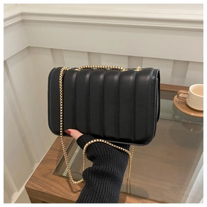 Detail of black quilted shoulder bag with golden chain strap in elegant cafe setting