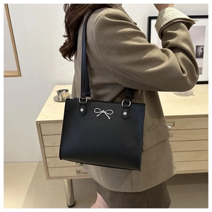 Detail view of the silver bow hardware on a black leather tote bag worn over the shoulder