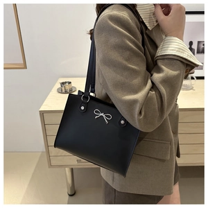 Close-up of black leather shoulder bag featuring a silver bow metal charm detail