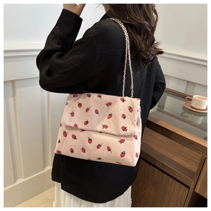 Detail of pink corduroy shoulder bag with red strawberry print and gold chain strap