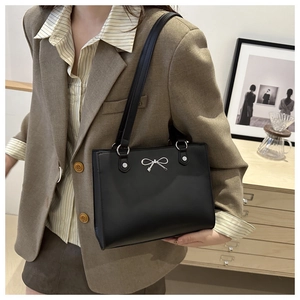 Detail of minimalist black tote bag with silver bow hardware and matte finish texture