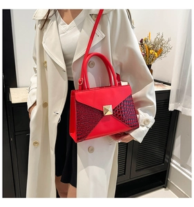 Detail of red leather crossbody bag featuring gold pyramid stud and croc-effect texture