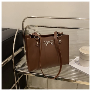 Detailed view of dark brown leather tote with a silver metal bow accent on a shelf