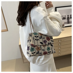 Detailed view of cream woven crossbody bag with colorful floral embroidery and gold chain