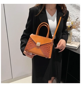 Detail of orange handbag showing crocodile texture side panels and square metal clasp