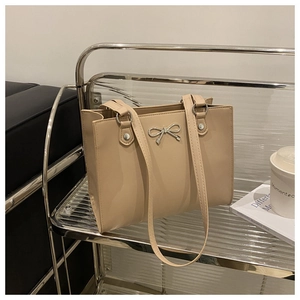 Detailed view of beige tote bag featuring a silver metal bow and pleated side design