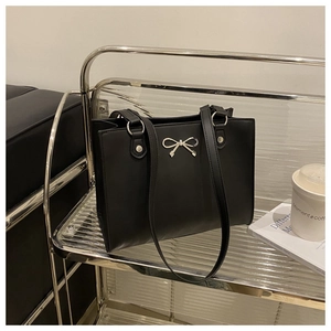 Detail of black tote bag with silver bow accent on an industrial metal shelf