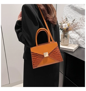 Detail of an orange-brown shoulder bag with faux crocodile skin texture and gold buckle