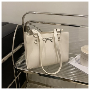 Detail of cream white PU leather tote bag with silver metal bow buckle on a metal shelf