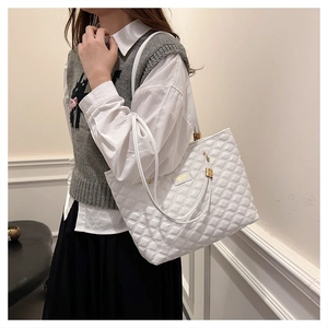 Close-up of white quilted tote bag featuring a gold metal brand plate and slim strap
