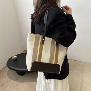 Detail of striped canvas tote bag showing dark brown leather bottom and reinforced handle rivets