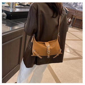 Sac bandoulière vintage marron avec boucles métalliques porté par un mannequin en café