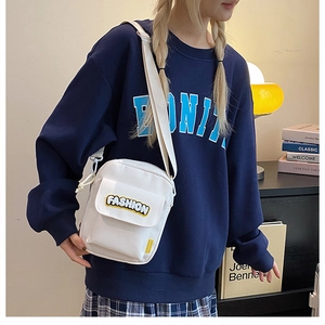 White canvas crossbody bag with FASHION print shown on model in a casual indoor setting