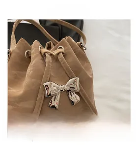 Detail of the warm apricot drawstring bucket bag featuring a silver metal bow and pleated leather
