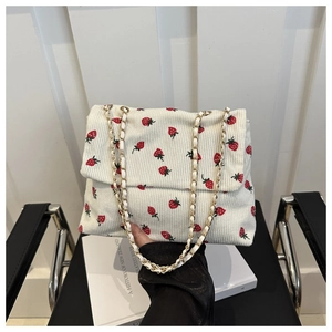 Close-up of white corduroy shoulder bag featuring red strawberry print and gold chain strap
