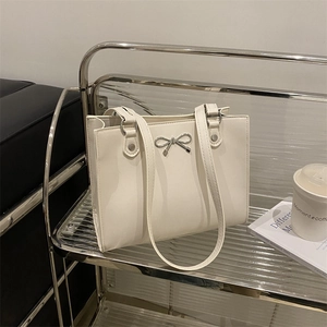 Chic cream leather tote bag with silver bow detail in a modern minimalist setting