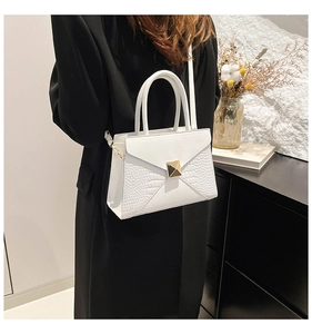 Detail of white envelope bag with crocodile texture and gold hardware on black blazer
