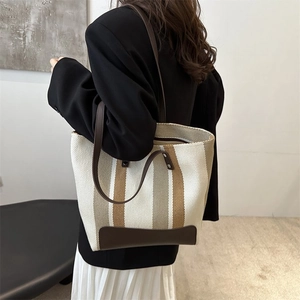 Detail of canvas tote bag showing striped pattern and brown leather straps on model