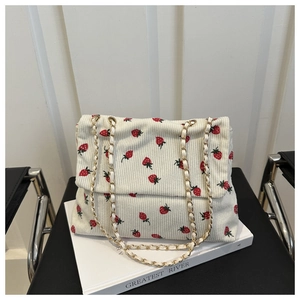 Detail of white corduroy shoulder bag featuring red strawberry embroidery and chain strap